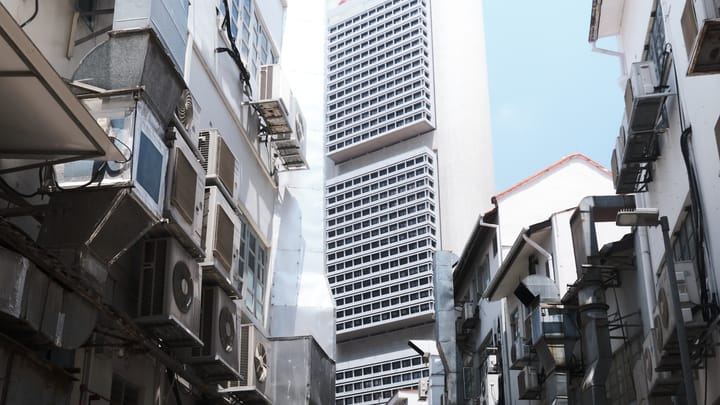 A Singapore back alley walled with air-conditioning units, a modernist tower rising between the shophouses